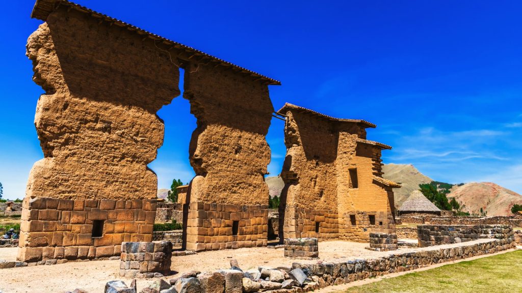 Vista frontal del monumental Templo de Wiracocha Raqchi con sus columnas de adobe y base inca de piedra, bajo un cielo azul brillante.