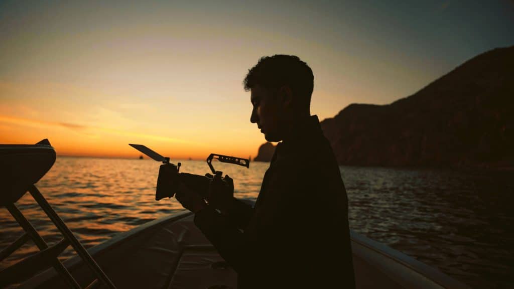 Silueta de fotógrafo con cámara en bote, capturando un vibrante atardecer sobre el agua. Consejos para fotos en el Lago Titicaca.